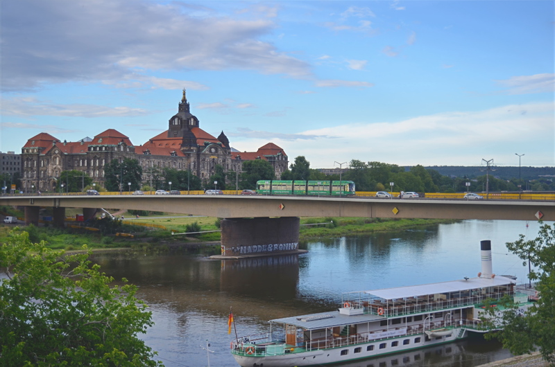 1 - A view across the Elbe River in Dresden, featuring the Carola Bridge carrying a green tram, with the grand Saxon State Chancellery in the background and a traditional paddle steamer